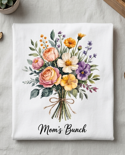 Floral design on a white towel with 'Mom's Bunch' text, placed on a textured surface.