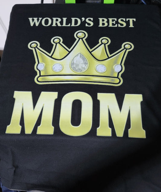 Black shirt with gold crown and 'World's Best Mom' text worn by a person, with shoes and a bag in the background.