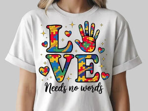 White t-shirt with colorful 'LOVE Needs No Words' design featuring puzzle pieces on a black background.