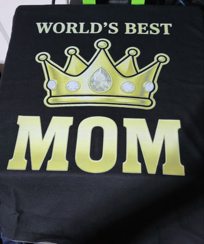 Black shirt with gold crown and 'World's Best Mom' text worn by a person, with shoes and a bag in the background.
