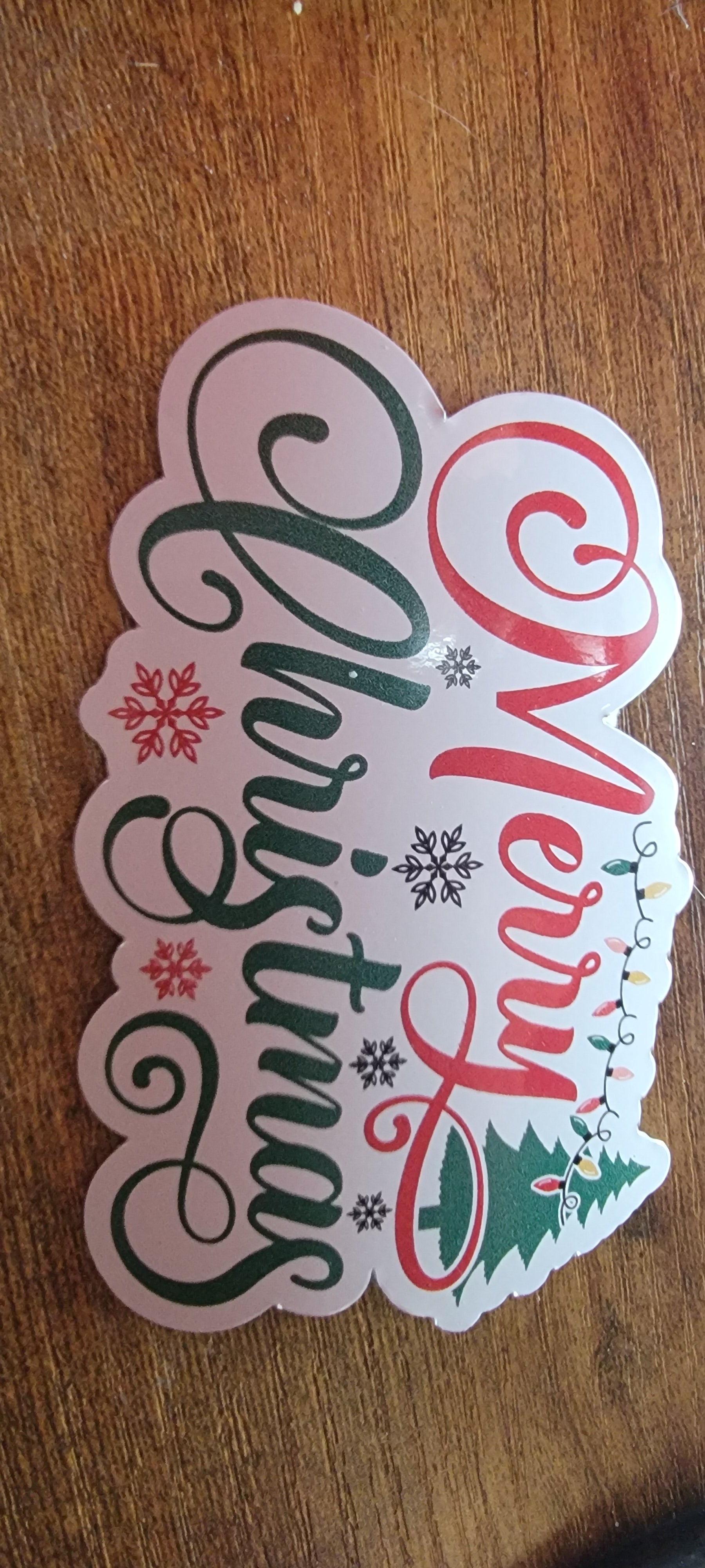 Christmas-themed sticker with 'Merry Christmas' text on a wooden surface